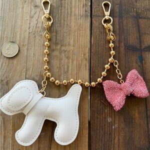 White dog on gold ball keychain with adorable pink bow attached .